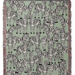May include: A woven throw blanket featuring a repeating pattern of zebras in black and white on a light green background. The blanket has a fringed edge in various colors. This decorative blanket is suitable for a bed or sofa.