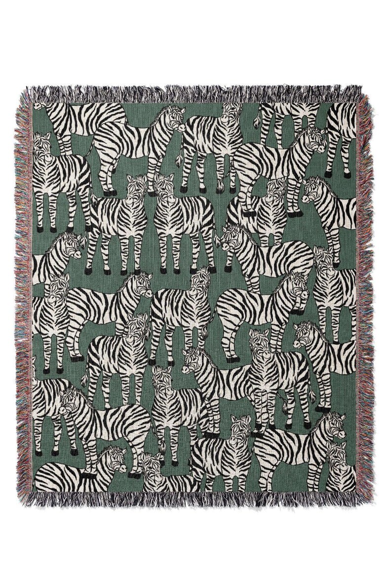 May include: A woven throw blanket featuring a repeating pattern of zebras in black and white against a green background. The blanket has a fringed edge with a mix of colors. This decorative blanket is suitable for home decor.