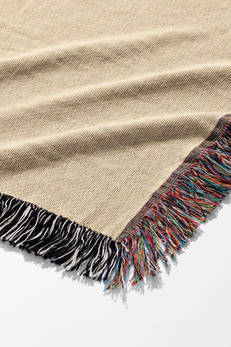 K&ouml;nnte beinhalten: Beige gewebte Decke mit farbenfrohem Fransenrand. Die Decke hat ein strukturiertes Aussehen und einen schwarz-wei&szlig;en Fransen an einer Seite. Die andere Seite hat einen lebendigen, mehrfarbigen Fransen.
