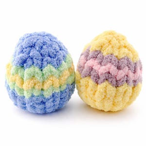 May include: Two fluffy, egg-shaped decorations. One is blue with green and yellow stripes. The other is yellow with pink and purple stripes. These soft, textured eggs are likely for Easter or spring decor.