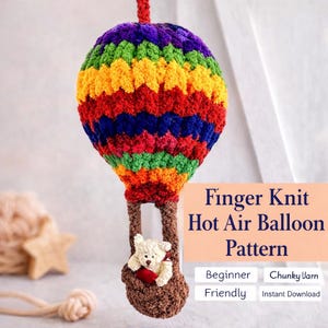 Könnte beinhalten: Ein buntes, fingergestricktes Heißluftballonmuster. Der Ballon ist mit leuchtenden Regenbogenfarben gestreift und hat einen braunen Korb mit einem kleinen Teddybären. Der Text auf dem Bild lautet "Finger Knit Hot Air Balloon Pattern".