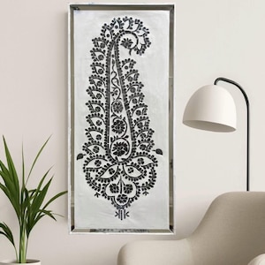 May include: A framed wall art piece featuring a large, black paisley design on a white background. The paisley is intricately detailed with floral and curved patterns. The frame is a simple, silver-toned rectangle. The artwork is displayed in a modern living space.