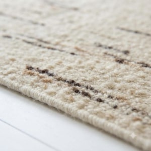 Pode incluir: Um tapete texturizado com pelo espesso na cor creme, apresentando estrias horizontais intermitentes de fibras castanho-escuras e bronzeadas tecidas por toda a superfície. O tapete possui uma construção densa e em laço com uma borda.