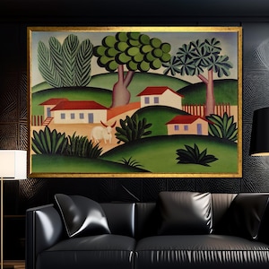 May include: A framed landscape painting with a gold frame. The artwork depicts a rural scene with rolling green hills, white houses with red roofs, and a white cow. Trees and bushes are scattered throughout the landscape.