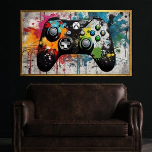 Könnte beinhalten: Gerahmtes Kunstwerk mit einem stilisierten Xbox-Controller-Design. Der Controller ist schwarz mit farbenfrohen Farbspritzern in Blau, Grün, Gelb und Orange. Das Kunstwerk ist vor einem weißen Hintergrund platziert und goldfarben gerahmt.