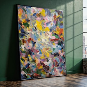 Puede incluir: Gran pintura abstracta enmarcada. La obra presenta una vibrante mezcla de colores, incluyendo amarillo, azul, rosa y rojo, aplicados con pinceladas visibles. La pintura se apoya en una pared verde, con una ventana en el fondo.