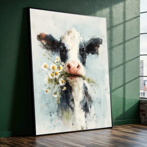May include: A framed watercolour painting of a cow with a black and white coat, holding a bouquet of white daisies in its mouth. The cow has a pink nose and is set against a light blue background. The artwork is displayed in a room with a green wall.