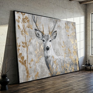 May include: Large framed canvas art depicting a deer with grey fur and gold antlers. The background is a textured grey with gold leaf accents. The artwork is displayed in a room with a wooden floor and a concrete wall.