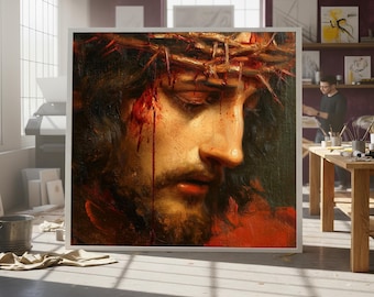 Pode incluir: Pintura emoldurada de um homem com barba e coroa de espinhos, com sangue escorrendo pelo rosto. A obra de arte é exibida em um estúdio de arte, com uma pessoa trabalhando ao fundo.
