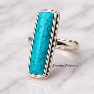 Könnte beinhalten: Ein silberner Ring mit einem rechteckigen türkisfarbenen Stein. Der Stein hat eine rissige Textur und ist in eine silberne Lünette gefasst. Der Ring liegt auf einer weißen Marmoroberfläche. Der Text "Sanwariya Seth Jewelry" ist sichtbar.