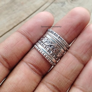 Op de afbeelding: Een verzameling zilveren ringen gestapeld op een vinger. De ringen hebben verschillende ontwerpen, waaronder bloempatronen, kralenranden en getextureerde banden. De ringen worden op een hand getoond, waarbij de verschillende stijlen en texturen worden getoond.