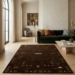 May include: A rectangular, dark brown rug with a patterned border and scattered geometric designs in various colors. The rug is placed on a light-colored wooden floor in a living room setting. The text "ShaigaArts" is visible on the rug.