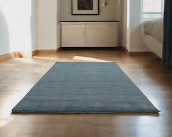 May include: A rectangular, solid blue rug lies on a hardwood floor. The rug is the focal point of the room, with a simple, textured design. The room has a neutral color palette, with natural light illuminating the space.