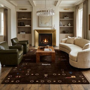 May include: A living room with a brown patterned rug, a curved beige sofa, and two green leather armchairs. A fireplace with a gold frame and a crystal chandelier add elegance. The room has wooden floors and built-in bookshelves.