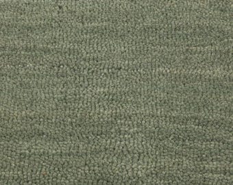 Pode incluir: Close-up de um tapete verde sálvia texturizado. O tapete tem uma pilha densa e em laço, criando uma aparência macia e felpuda. A cor é um tom suave e terroso, adequado para vários estilos de design de interiores. A textura do tapete sugere conforto e calor.