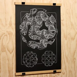 May include: Black poster with white geometric designs, mounted with wooden bars and black clips. The poster features a large, complex circular pattern at the top and two smaller circular patterns below. The background is a light wood grain.