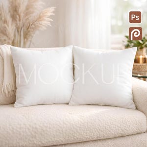 以下が含まれることがあります： クリーム色のソファに2つの正方形の白いクッションが置かれています。クッションは無地で滑らかで、ソファのテクスチャード加工された生地とは対照的です。シーンは柔らかく自然な光に包まれ、居心地の良いリビングスペースを連想させます。