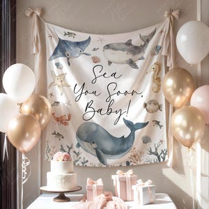 Pode incluir: Uma cena de ch&aacute; de beb&eacute; com uma faixa com criaturas marinhas e o texto "Sea You Soon, Baby!". Bal&otilde;es dourados, brancos e rosa decoram a sala. Um bolo de dois andares e presentes embrulhados est&atilde;o em uma mesa.