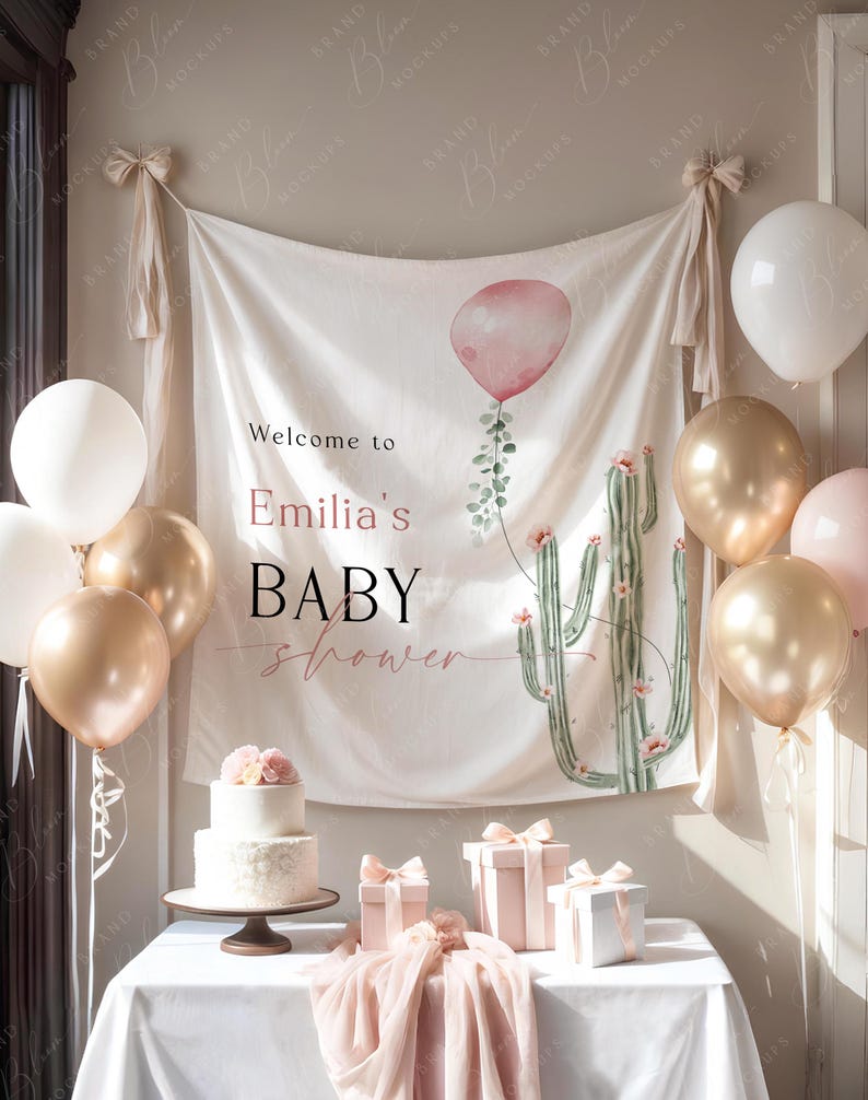 Pode incluir: Uma cena de ch&aacute; de beb&eacute; com uma faixa que diz "Welcome to Emilia's BABY shower". A faixa apresenta um cacto em aquarela e um bal&atilde;o rosa. Bal&otilde;es dourados, brancos e rosa decoram o quarto. Um bolo de dois andares e presentes embrulhados est&atilde;o em uma mesa.