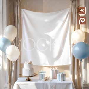 May include: A styled scene with a white two-tiered cake on a gold stand, complemented by pastel balloons and wrapped gift boxes with ribbons. A white backdrop hangs behind the table, creating a soft, elegant atmosphere.