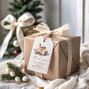 May include: A wrapped gift box with a tag that reads "Thank you" for a baby shower. The box is wrapped in brown paper and tied with a burlap ribbon. The tag features a watercolor illustration of a mug of hot cocoa.