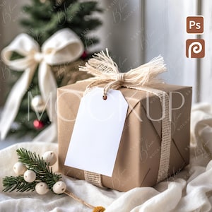 May include: A wrapped gift box with a blank white tag, decorated with a burlap ribbon and bow. A small Christmas tree and decorative sprigs with white berries and yellow pom-poms are in the background. The gift box is wrapped in brown paper.