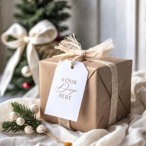 May include: A wrapped gift box with a white tag that reads "YOUR Design HERE". The box is wrapped in brown paper and tied with a burlap ribbon and twine. A small Christmas tree and decorative sprig are in the background.