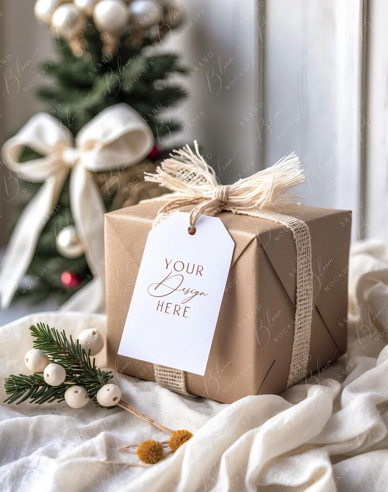 May include: A wrapped gift box with a white tag that reads "YOUR Design HERE". The box is wrapped in brown paper and tied with a burlap ribbon and twine. A small Christmas tree and decorative sprig are in the background.