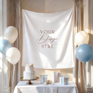 May include: A staged event scene with a white tablecloth, cake, gifts, and balloons. A two-tiered white cake sits on a gold cake stand. The backdrop features a white banner with the text "YOUR Design HERE". Balloons in white and blue are arranged around the scene.