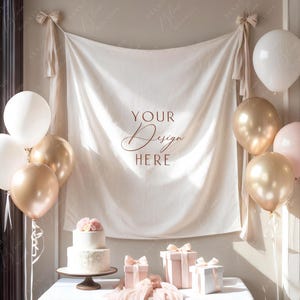Pode incluir: Uma cena festiva com uma toalha de mesa branca, bal&otilde;es e um bolo. O fundo apresenta uma faixa com o texto "YOUR Design HERE". Caixas de presente e tecido drapeado real&ccedil;am o ambiente festivo. Bal&otilde;es dourados e brancos est&atilde;o dispostos.