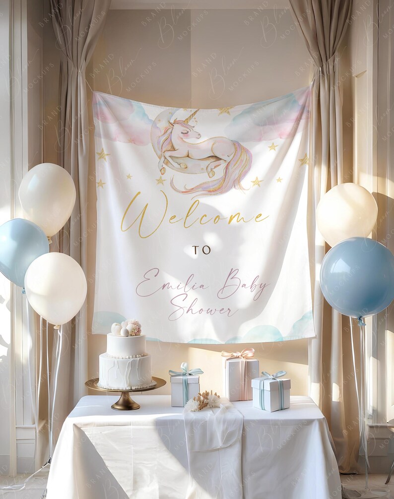 May include: A baby shower setup with a white tablecloth, balloons, and a banner reading "Welcome to Emilia Baby Shower." A two-tiered cake is on a gold stand, with gifts on the table. The banner displays a unicorn illustration.