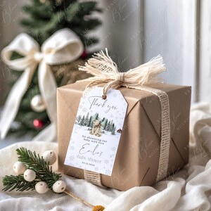 May include: A wrapped gift in brown paper with a tag that says "Thank you" and "baby shower". The tag features a winter scene with a bear. The gift is tied with a burlap ribbon and a white bow.