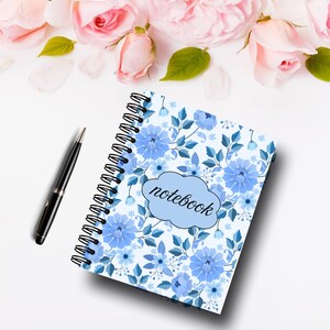 May include: A spiral-bound notebook with a light blue floral design featuring blue flowers and leaves. The word "notebook" is written in a cloud-shaped design. A black pen is placed next to the notebook.