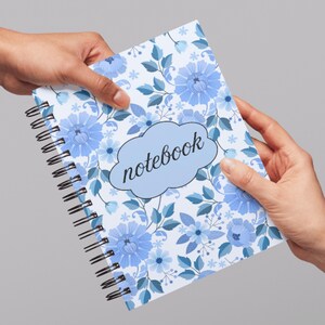 May include: A spiral-bound notebook with a floral design. The cover features blue flowers and leaves on a white background. The word "notebook" is written in a light blue cloud-shaped text box.