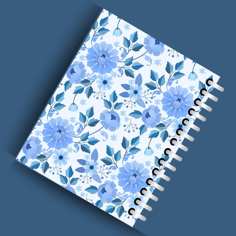 May include: A spiral-bound notebook with a floral pattern. The cover features a repeating design of blue flowers and leaves on a white background. The notebook's spiral binding is white, and the overall aesthetic is soft and feminine.