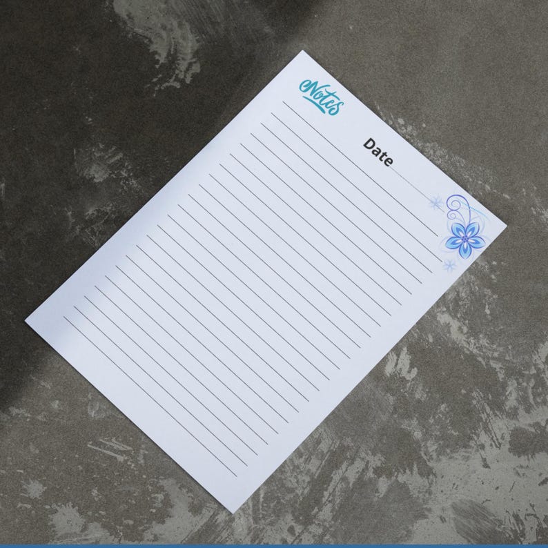 May include: White lined notepad with the word "Notes" in teal script at the top left. The word "Date" is printed below the notes. A blue floral design is in the top right corner. The notepad is angled on a gray surface.