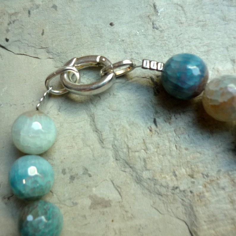 May include: A silver clasp with a chain attached to a necklace of blue and green agate beads.