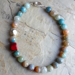 May include: A multi-colored agate gemstone necklace with a silver clasp. The necklace features a variety of colors, including blue, green, orange, and red. The beads are round and have a smooth, polished finish.