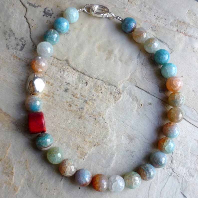 May include: A multi-colored agate gemstone necklace with a silver clasp. The necklace features a variety of colors, including blue, green, orange, and red. The beads are round and have a smooth, polished finish.