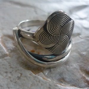 May include: A silver ring with a swirling, textured design. The ring is made of two bands that are intertwined.
