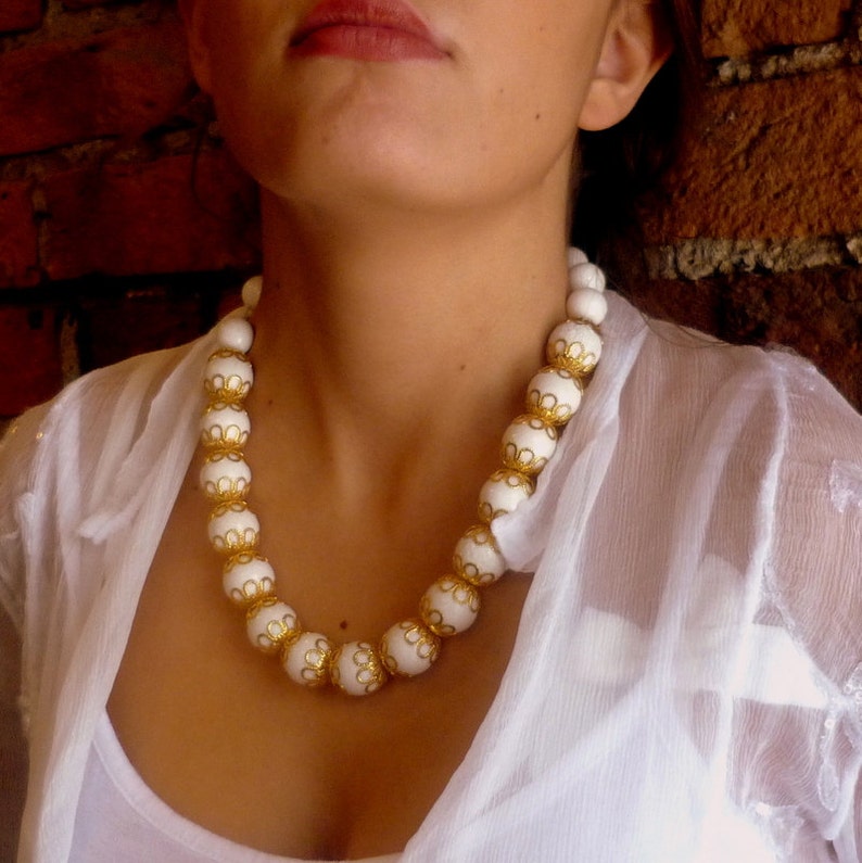 May include: A white beaded necklace with gold accents. The beads are round and have a delicate floral design.