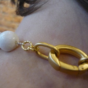 Puede incluir: Un collar de cuentas de cer&aacute;mica blanca con un cierre dorado. El collar est&aacute; hecho de cuentas grandes y redondas.