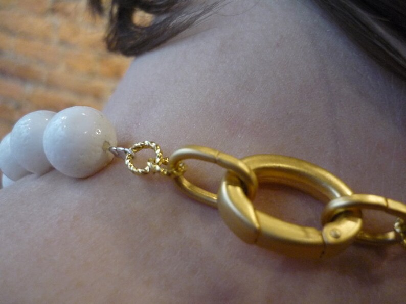 Puede incluir: Un collar de cuentas de cer&aacute;mica blanca con un cierre dorado. El collar est&aacute; hecho de cuentas grandes y redondas.