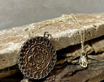 May include: A gold and silver necklace with a round pendant featuring a detailed mandala design.