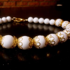 May include: White beaded necklace with gold filigree accents. The beads are round and have a textured surface.