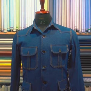Op de afbeelding: Een blauwe spijkerjas met lange mouwen, een kraag en vier voorzakken met knoopsluiting. De jas is voorzien van contrasterende bruine stiksels, een centrale knoopsluiting en wordt getoond op een paspop met het nummer 40.