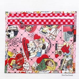 May include: Pink zippered pouch with a clear vinyl window. The pouch is decorated with a repeating pattern of vintage Valentine's Day illustrations featuring children, hearts, and the text "You're just cut out for me".