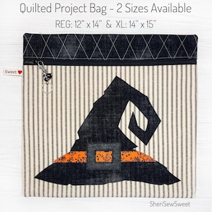 May include: A quilted project bag with a witch hat design. The bag is made of a striped fabric with a black and white pattern. The bag has a zipper closure and a small charm attached to the zipper. The bag is available in two sizes: 12" x 14" and 14" x 15".