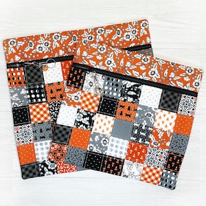 May include: Two orange and black patchwork zippered pouches with a floral print on the top. The pouches are made of fabric and have a quilted design.