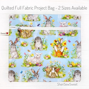 May include: A blue quilted zippered project bag with a white zipper and a repeating pattern of bunnies, lambs, and chicks in a spring garden setting. The bag has the text "SheriSewSweet" on the bottom.